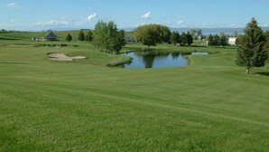 A golf course with a pond, trees, and a small building.