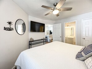 Relax in this spacious bedroom with a large bed, ceiling fan, and wall-mounted TV.
