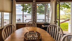 A wooden dining table with four chairs, a decorative tray, and a view of a lake with a dock and an American flag. - Seneca Sunsets - Awesome Lakeside Getaway Near Geneva! (Geneva)