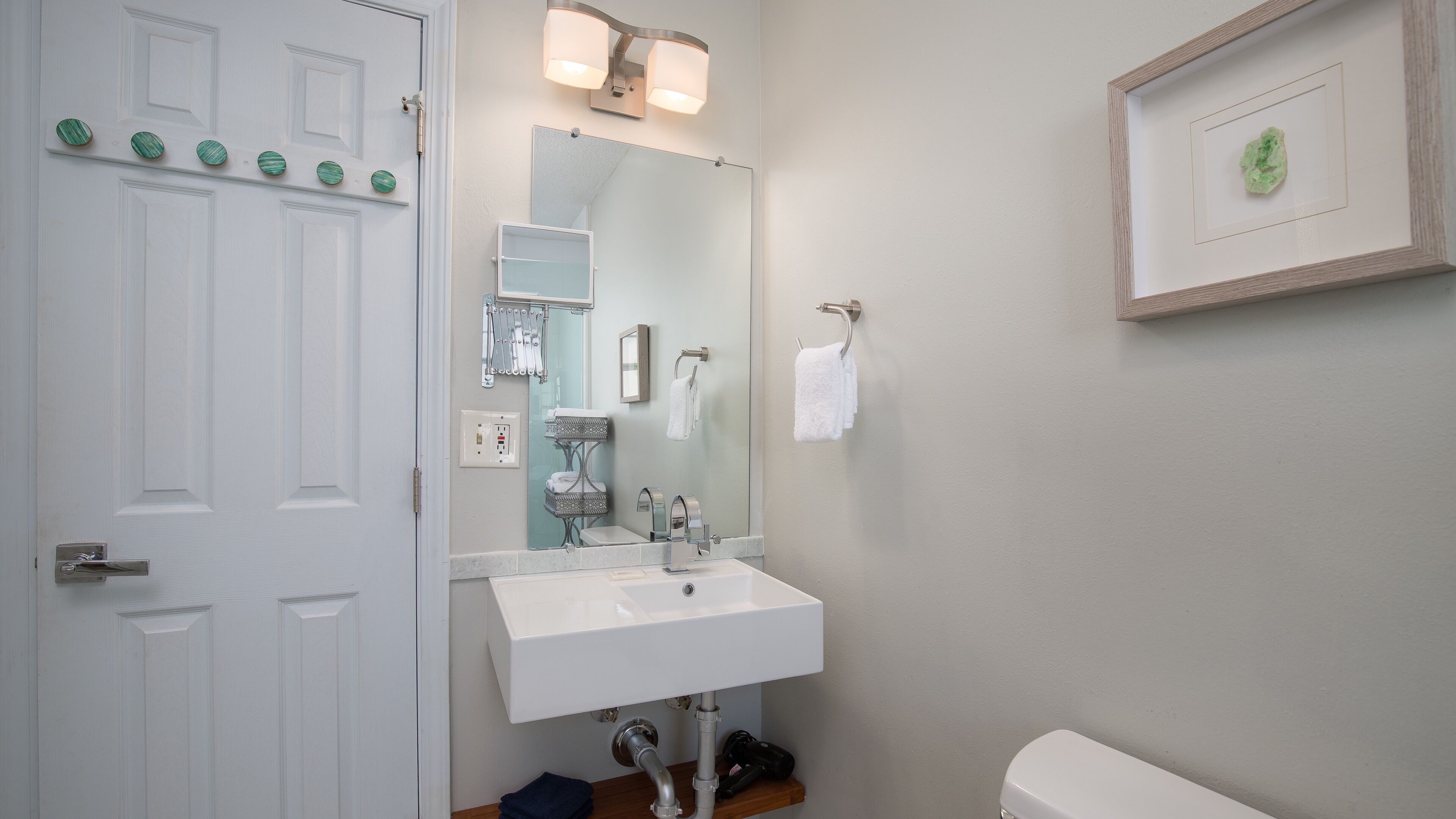A bathroom with a white sink, a mirror, and a framed picture on the wall.