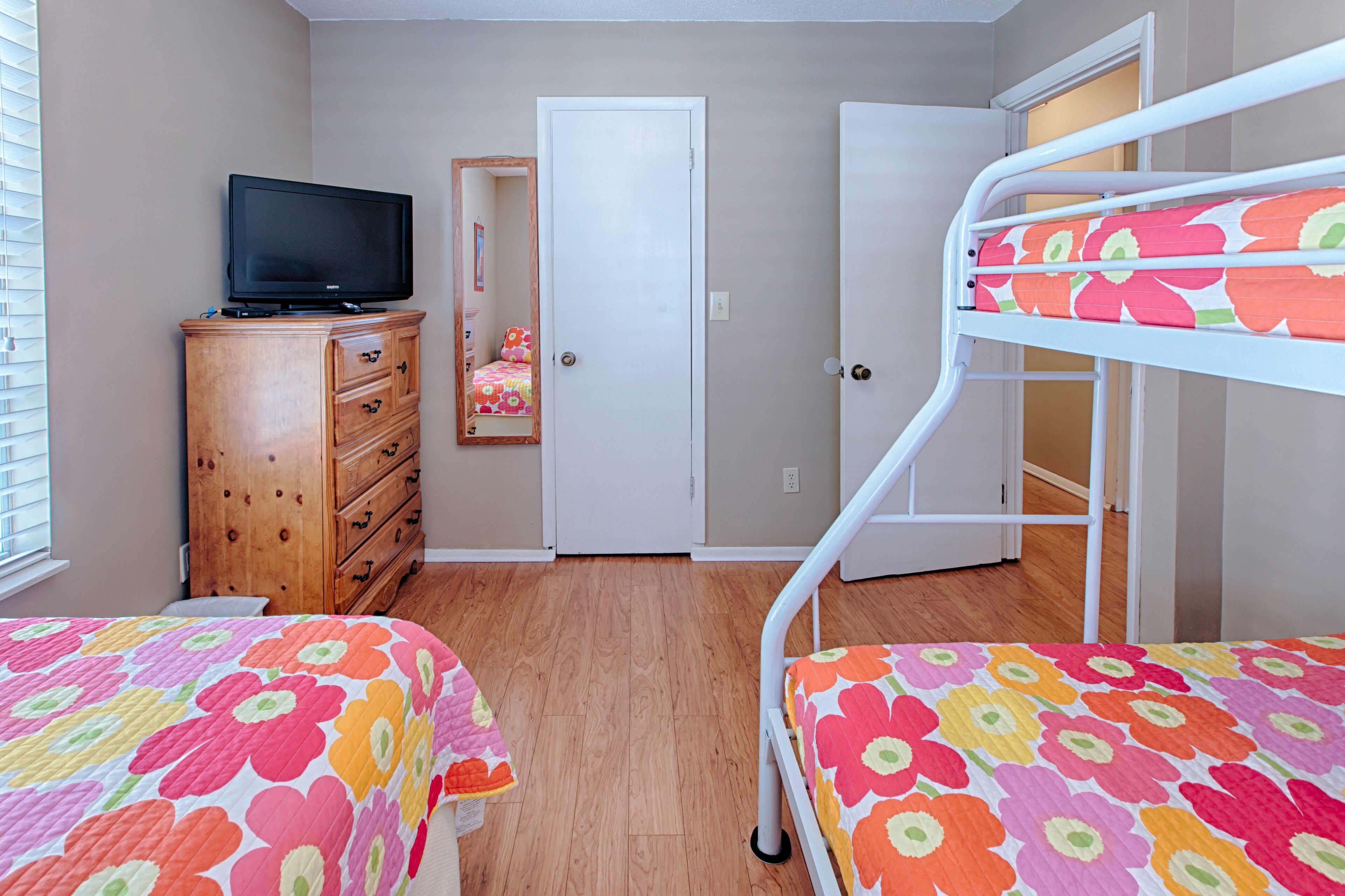 Un dormitorio con dos camas, un aparador, un televisor y una puerta.