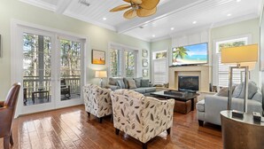 A spacious living room with hardwood floors, a ceiling fan, a fireplace, and a large TV.