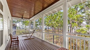 A covered wooden deck with a hammock, chairs, and a table.