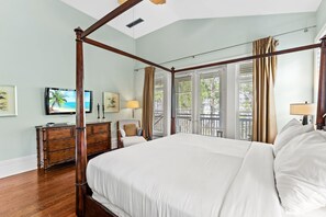A spacious bedroom with a four-poster bed, a wooden dresser, a television, and a balcony with a view of the city. - Golf Cart Included ~ Bay View ~ Screened Porch (Miramar Beach)