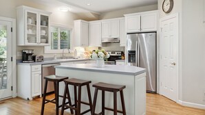 A modern kitchen with white cabinetry, a stainless steel refrigerator, and a central island with stools.