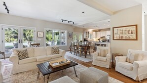 A spacious living room with a sofa, chairs, and a coffee table. There is a dining area with a table and chairs, and a kitchen in the background.