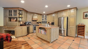 A kitchen with wooden cabinets, a stainless steel refrigerator, and a tiled floor. - 15 min from the Mont Tremblant Ski Hills, Perfect for Families and Friends ! (La Conception)