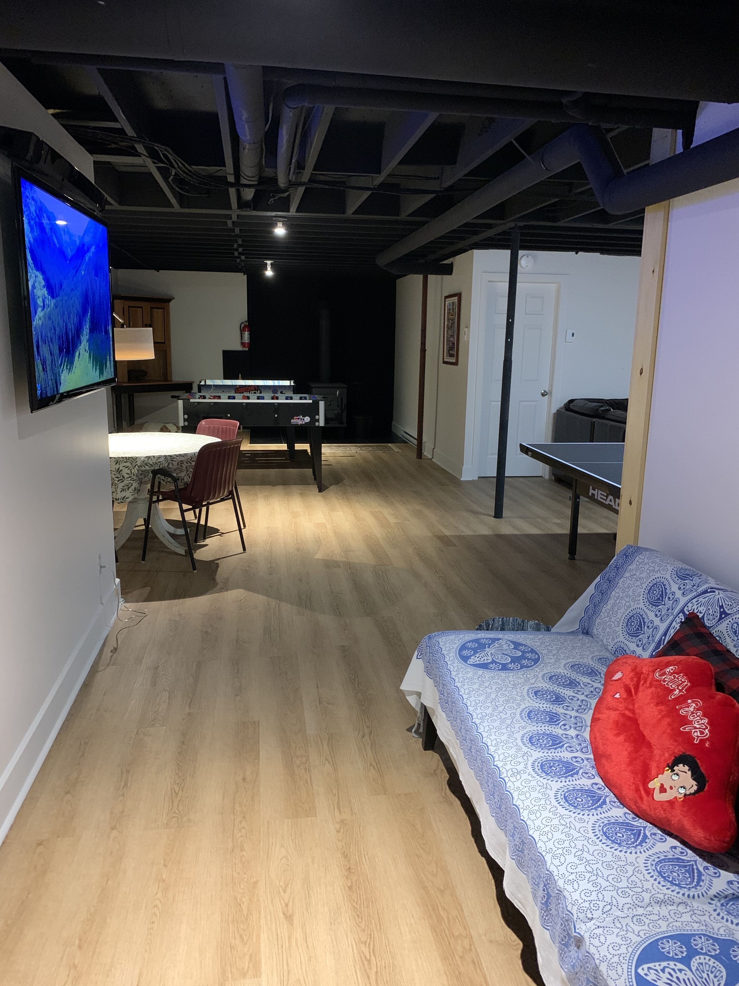 Ett rum med en säng, ett bord med stolar, ett bordtennisspel och en tv som är monterad på väggen.