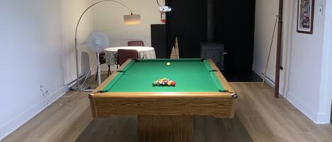 A pool table in a room with wooden flooring, a ceiling fan, and a lamp.