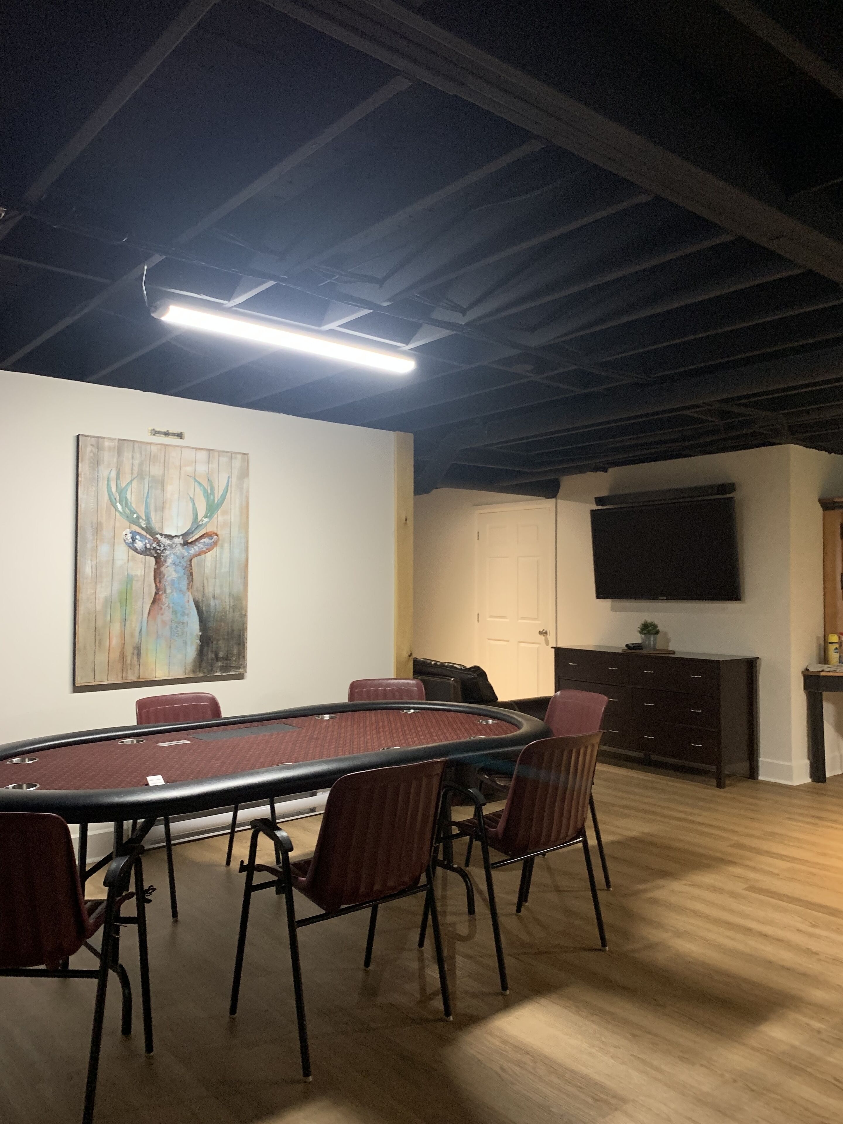 Une salle de conférence avec une longue table, des chaises, un tableau représentant un cerf, un téléviseur et un meuble.