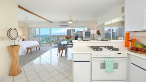 A modern hotel room with a balcony, a kitchenette, and a dining area with a city view.