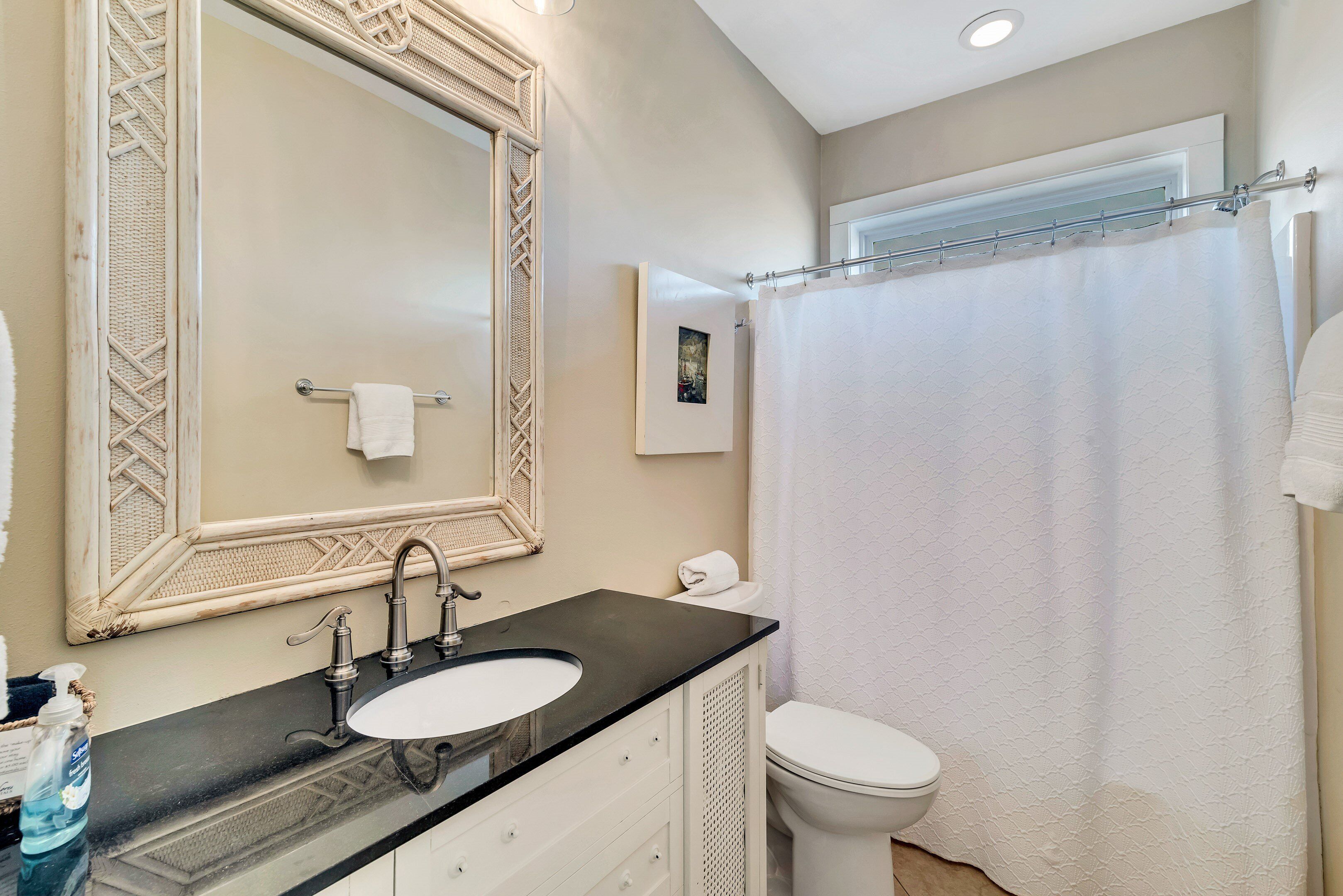 A bathroom with a large mirror, a sink, a toilet, and a shower curtain.