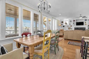A dining area with a wooden table and chairs, a chandelier, and a view through large windows.