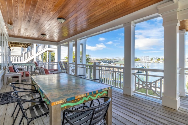A covered outdoor deck with a wooden ceiling, white railings, and a view of a body of water.