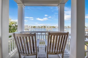 A wooden deck with two chairs and a table, overlooking a marina with boats and buildings.