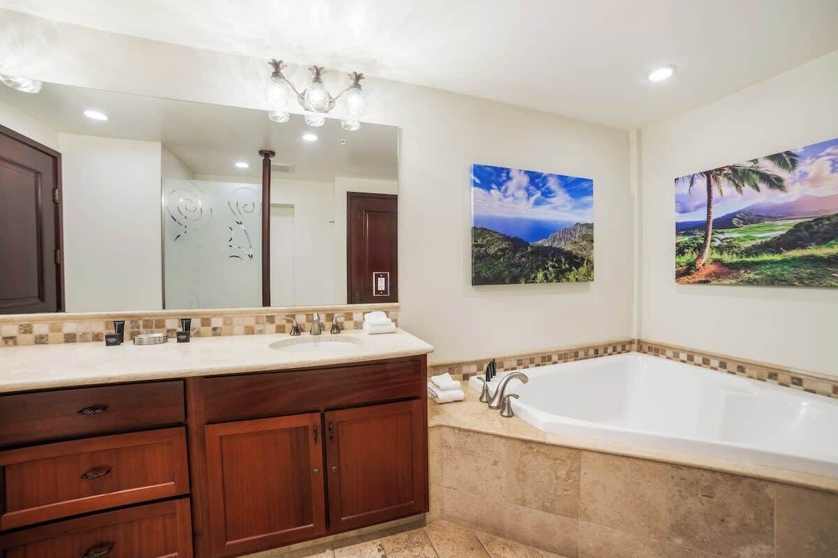 A bathroom with a large mirror, a bathtub, and two wall-mounted paintings.