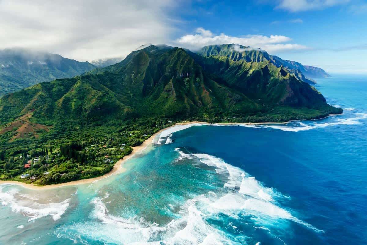 An aerial view of a coastal area with a mountain, clear blue waters, and a beach.