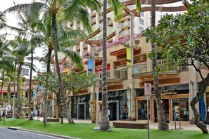 A multi-story hotel with balconies, palm trees, and a grassy area.