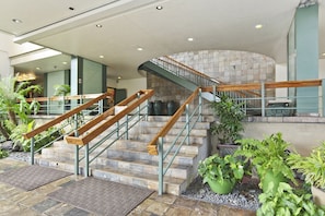Staircase flanked by potted plants, leading to a stone wall with a curved design.