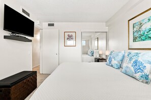 A hotel room with a large bed, a flat-screen TV mounted on the wall, a door leading to a bathroom, and a framed picture on the wall.