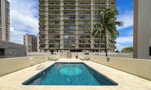 A swimming pool with a lifeguard stand, lounge chairs, and a high-rise building in the background.