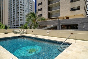 Una piscina con una postazione di salvataggio, sedie a sdraio e una palma.