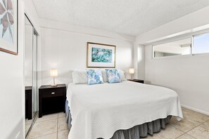 A bedroom with a large bed, two bedside tables, a nightstand, a framed picture on the wall, and a window.