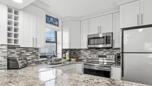 A modern kitchen with white cabinets, stainless steel appliances, a granite countertop, and a backsplash with gray tiles.
