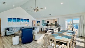 A spacious living area with a high ceiling, a dining table with chairs, a sofa, and a kitchen in the background.