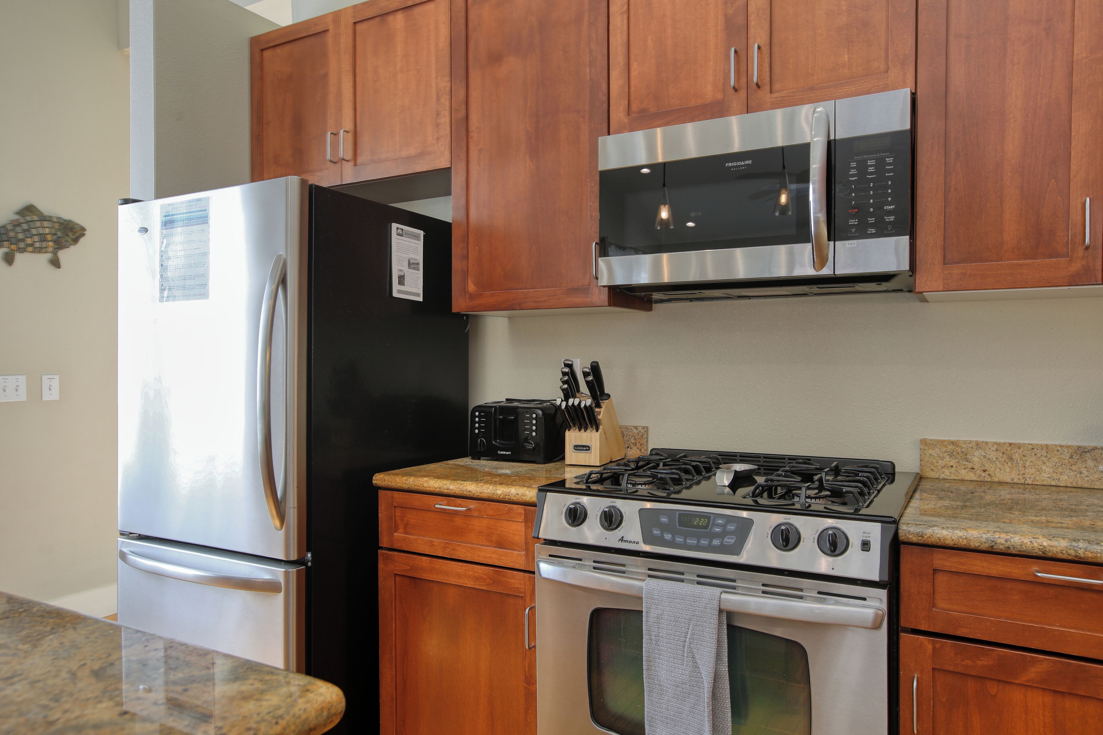 Una cocina con un refrigerador de acero inoxidable, un microondas, una estufa y gabinetes de madera.