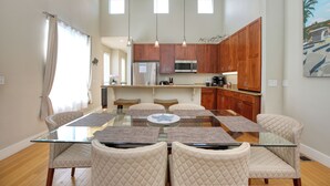 Une cuisine moderne avec des meubles en bois, une table à manger en verre et des luminaires suspendus.