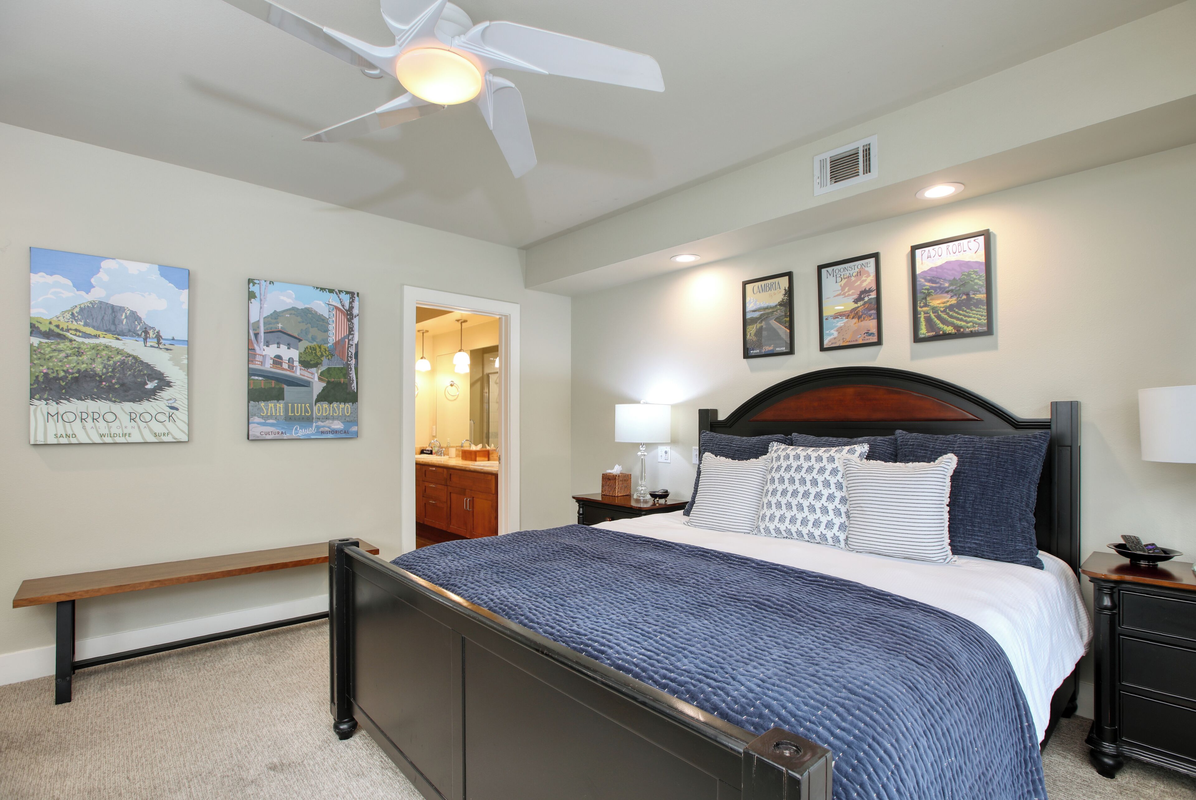 A bedroom with a bed, a bench, a ceiling fan, and wall art.