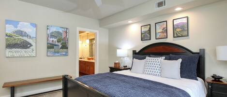 A bedroom with a bed, a bench, a ceiling fan, and wall art.