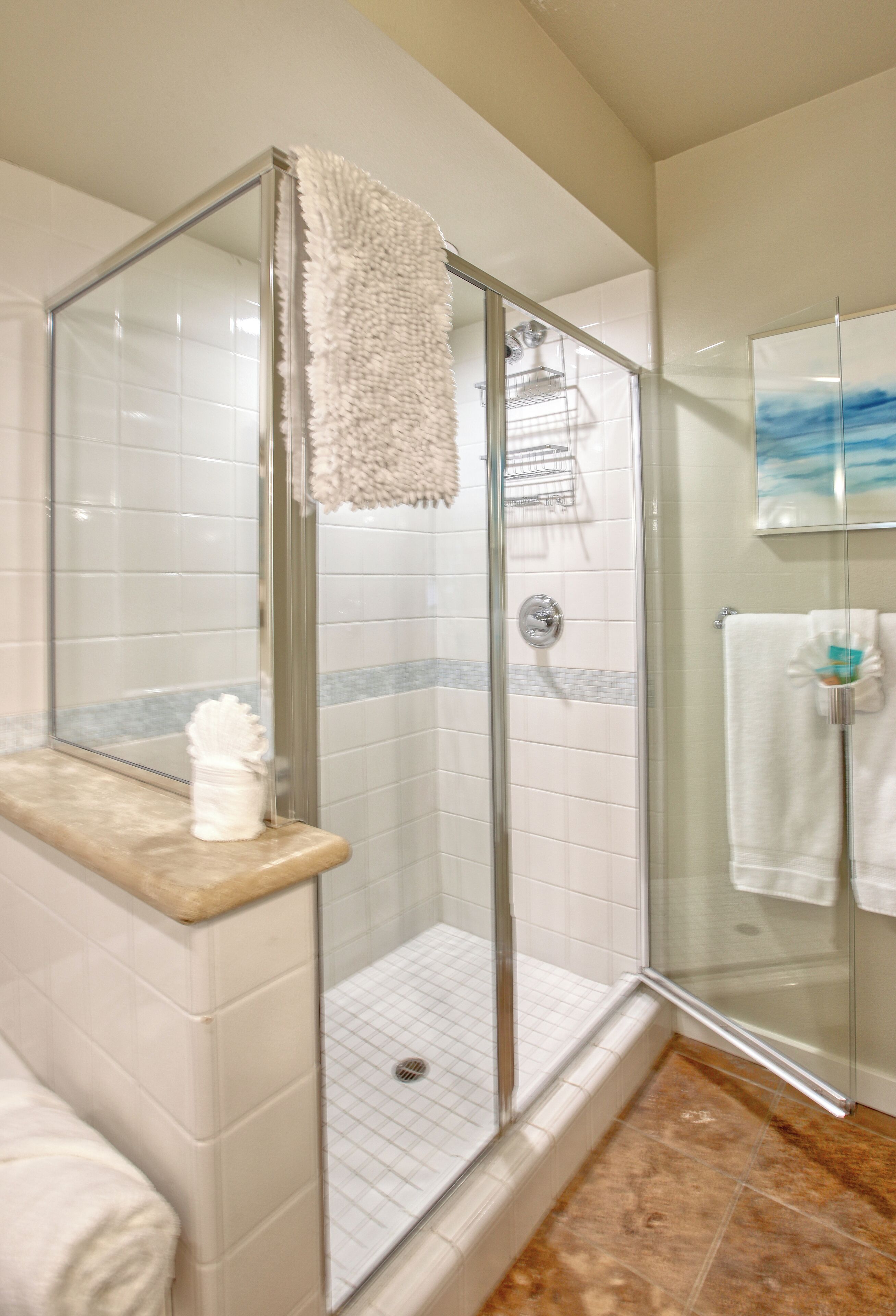 A glass-enclosed shower with a white towel on the counter and a towel rack in the adjacent room.