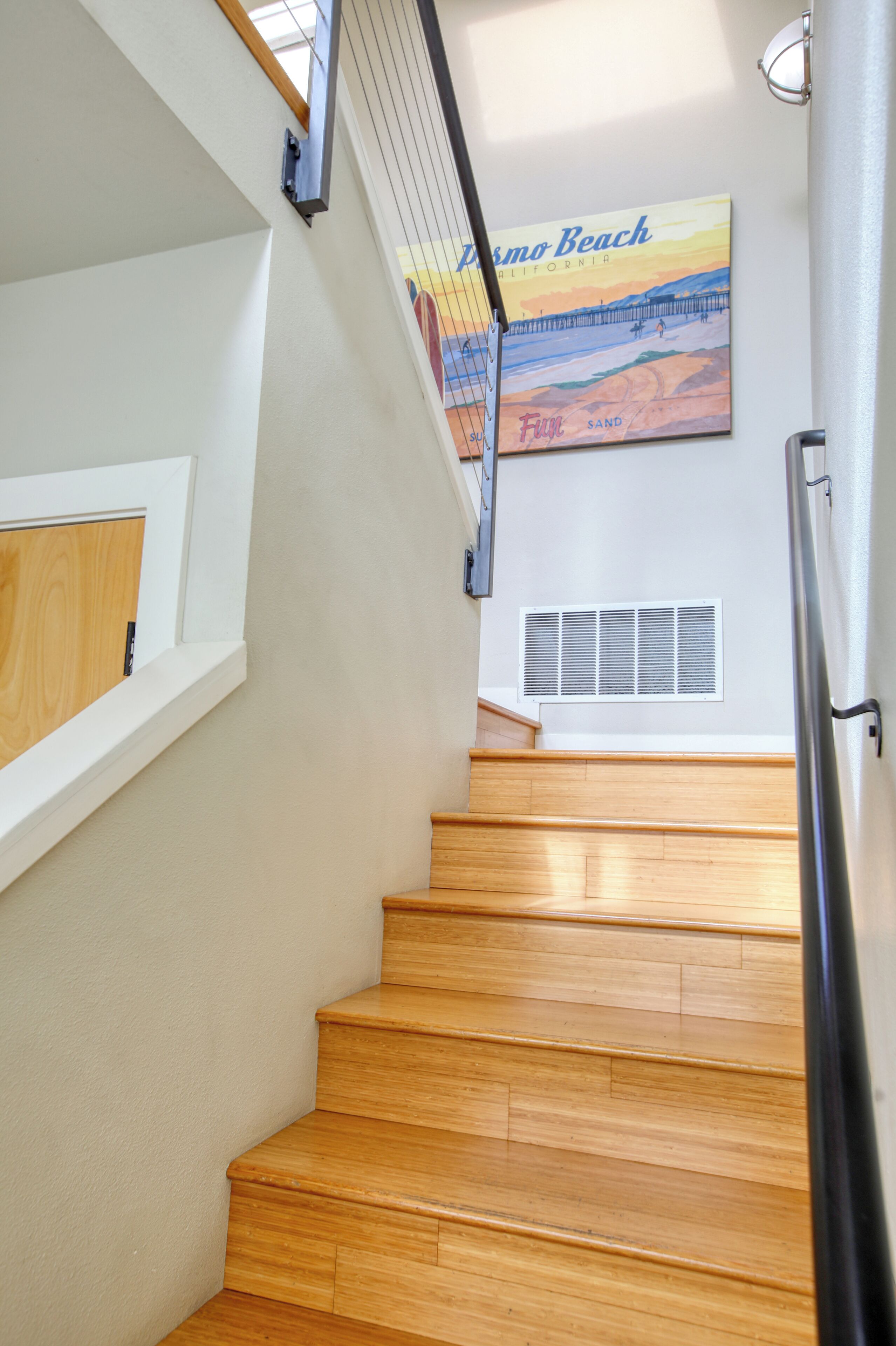 A wooden staircase with a handrail, a white wall, and a beach-themed poster.