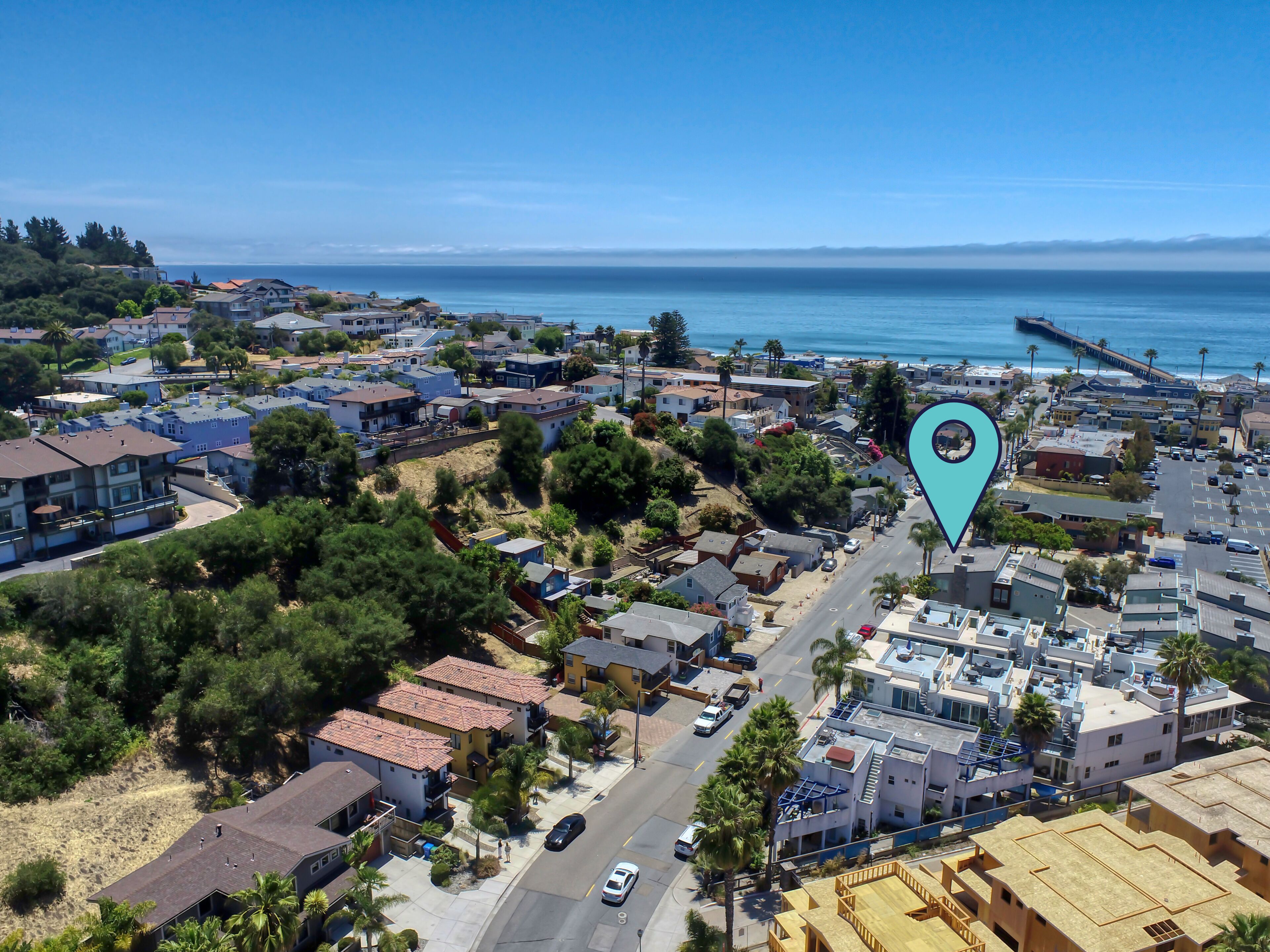 An aerial view of a coastal residential area with houses, a road, and a pier.