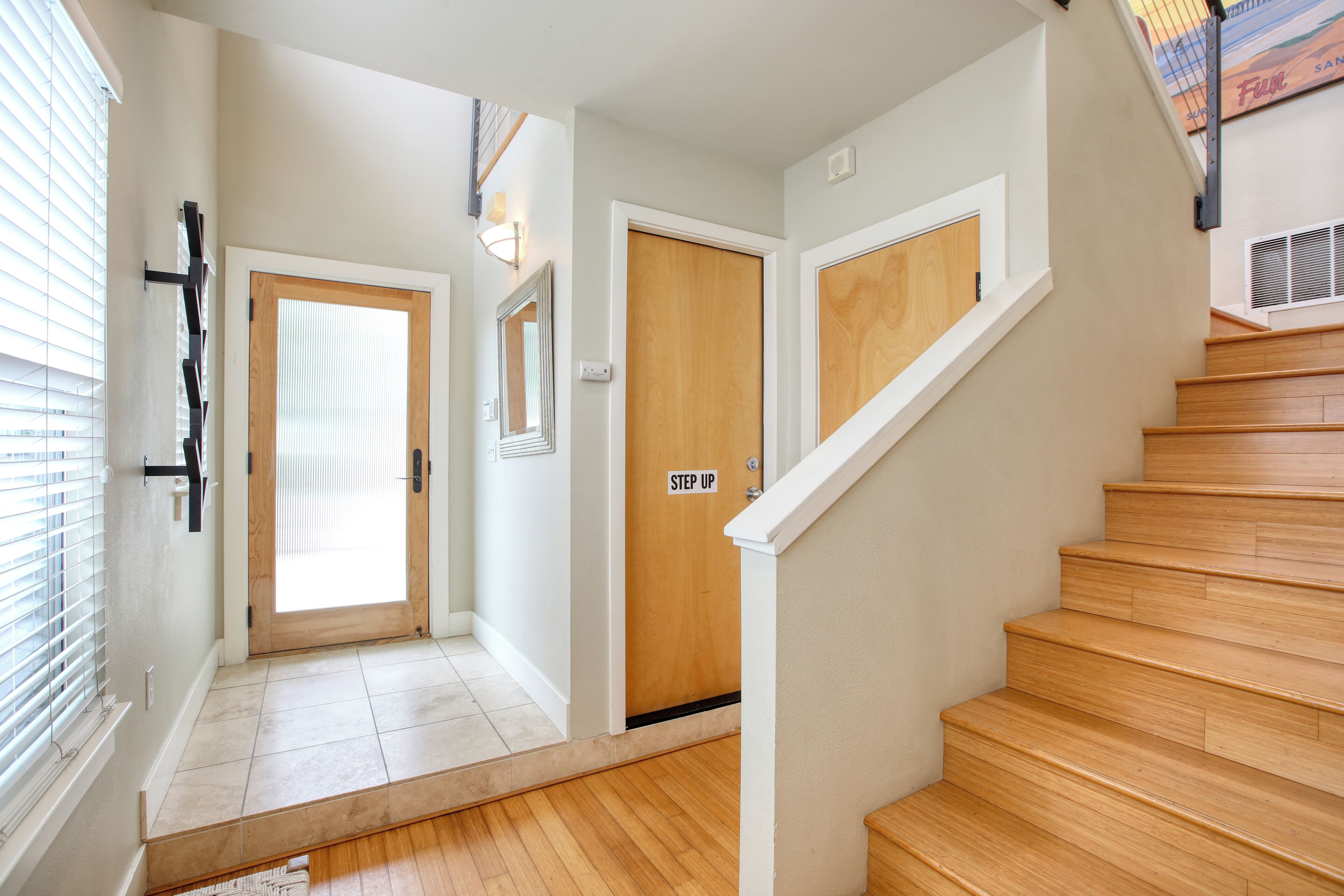 Eine Treppe mit Holzbodenstufen führt zu einer oberen Etage, eine Tür mit dem Schild 'STEP UP' und eine an der Wand befestigte Leuchte.