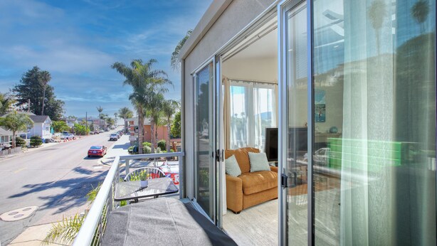 Un balcon avec une porte-fenêtre coulissante donnant sur un espace de vie comprenant un canapé et un téléviseur.