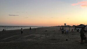 A beach with people walking and sitting, a clear sky, and a sunset. - Beautifully remodeled canal home, short walk from beach! Pet friendly, WiFi (Galveston)