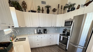 A modern kitchen with white cabinets, a stainless steel refrigerator, and a wooden floor. - Beautifully remodeled canal home, short walk from beach! Pet friendly, WiFi (Galveston)