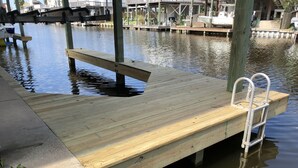 A wooden dock extending into a calm body of water, with a metal ladder on the right side. - Beautifully remodeled canal home, short walk from beach! Pet friendly, WiFi (Galveston)