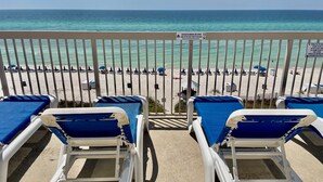Ein Balkon mit weißen und blauen Liegestühlen mit Blick auf einen Strand.