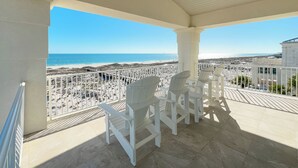 A covered balcony with white chairs and a view of the beach and ocean. - Kiva Grand by GSVR | Spectacular Beachfront Family Retreat w/ Pool & Hot Tub + FREE Activities/Golf (Gulf Shores)