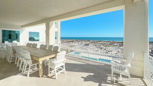 A covered outdoor area with a dining table and chairs, a pool, and a view of the beach and ocean. - Kiva Grand by GSVR | Spectacular Beachfront Family Retreat w/ Pool & Hot Tub + FREE Activities/Golf (Gulf Shores)