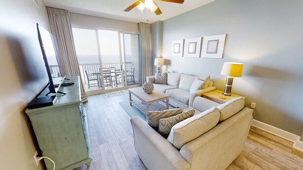 Een woonkamer met een bank, salontafel en een televisie op een meubel. Er is een balkon met uitzicht.