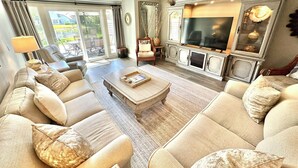 Un salón amplio con un televisor grande, asientos cómodos y vistas a través de puertas de cristal.