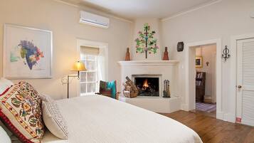 Un dormitorio con cama, chimenea, ventilador de techo y puerta que da a otra habitación.