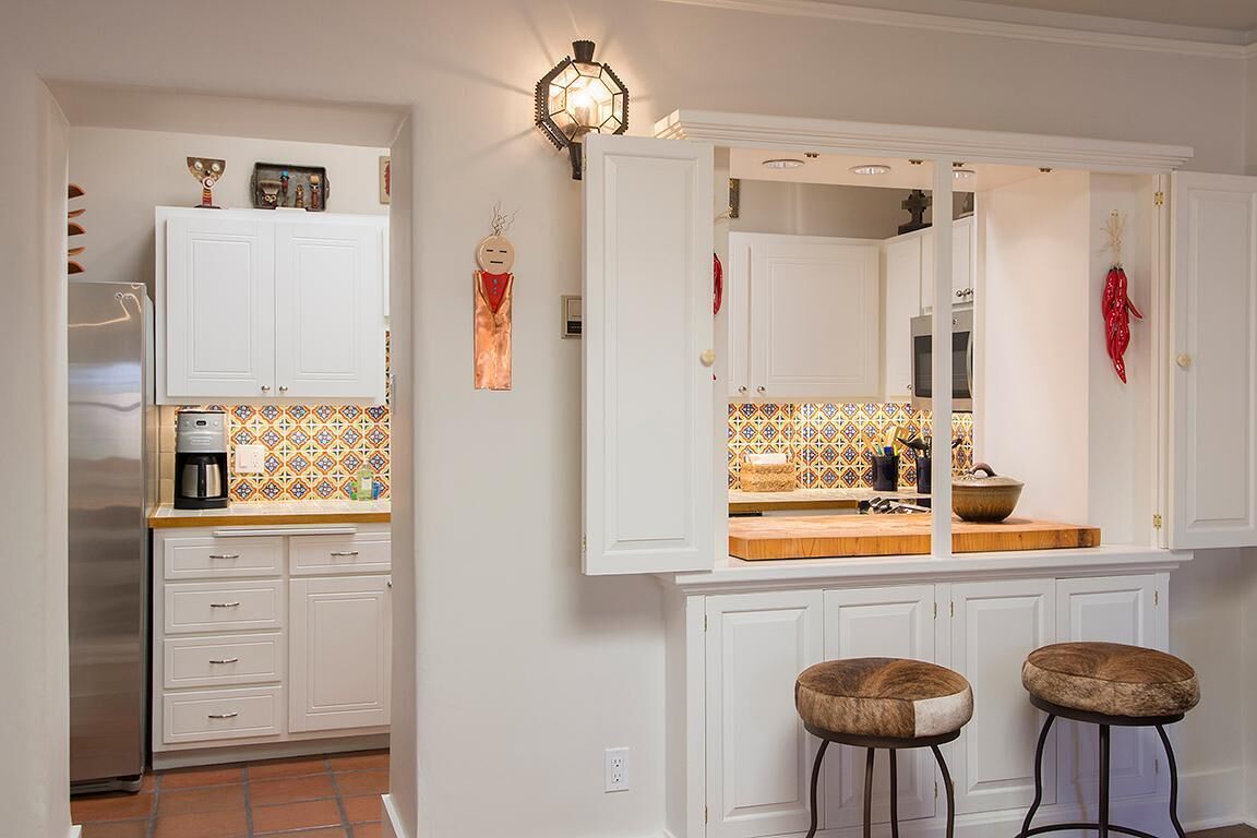 Una cocina con armarios blancos, salpicadero de azulejos y dos taburetes.