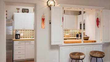 Una cocina con armarios blancos, salpicadero de azulejos y dos taburetes.