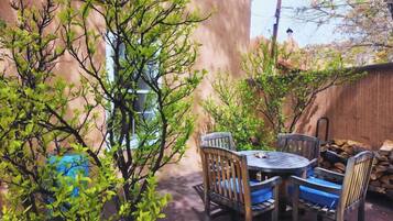 Un patio con una mesa redonda y sillas, rodeado de árboles y una cerca de madera.